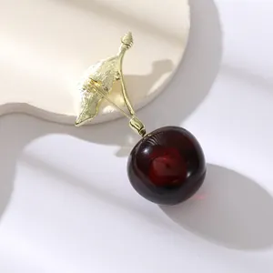 Broche cerise élégante avec feuilles dorées et perle en résine rouge sur support blanc