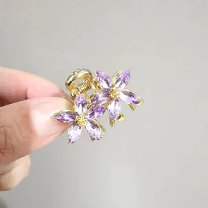 Gros plan d'une petite pince à cheveux dorée avec deux fleurs en cristal violet en main
