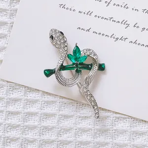 Detail of silver snake brooch with green crystals and rhinestones on a white fabric background