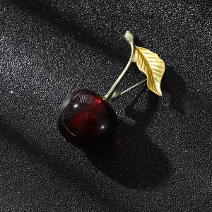 Détail de la broche cerise rouge avec feuille dorée et résine translucide sur fond noir