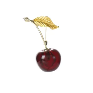 Broche cerise rouge élégante avec feuilles dorées sur un fond blanc minimaliste