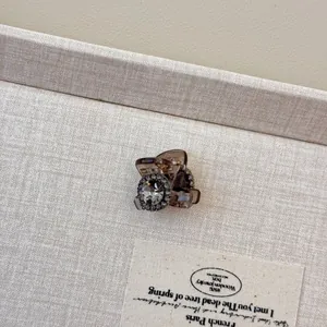 Close-up of a mini hair claw clip with rhinestones and grey gemstone on a jewelry tray