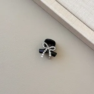 Detail of a black hair claw clip featuring rhinestone bow and pearl tassel accents
