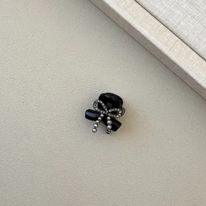 Elegant black claw clip with rhinestone bow and hanging pearl detail on beige leather
