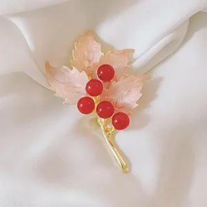 Elegant maple leaf brooch with pink enamel and red berries on a silk background
