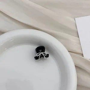 Detailed close-up of a mini black bow hair claw clip with silver rhinestone on white plate