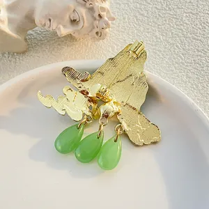 Vintage gold enamel landscape brooch with three green teardrop charms on a ceramic tray