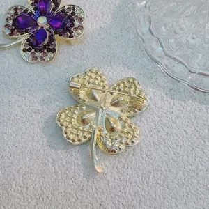 Green crystal four-leaf clover brooch set with purple rhinestones on a gold metal base