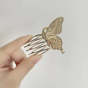 Golden butterfly 5-tooth metal hair comb for women shown held by a hand on a grey background