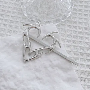 Detalle de pinza de pelo corazón llama Y2K plateada con acabado metálico pulido en tela
