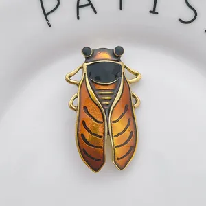 Vintage cicada insect brooch with orange gradient enamel and gold metal frame on a dish