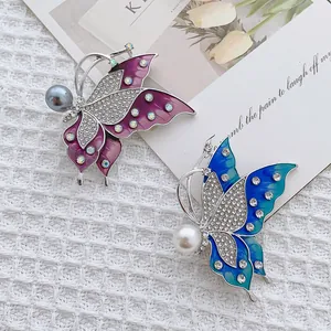 Elegant butterfly brooch set with enamel wings and pearls on a white textured background