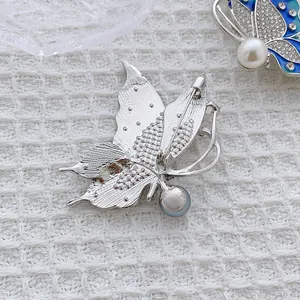 Luxury butterfly brooch with blue enamel, sparkling crystals and pearl on white fabric