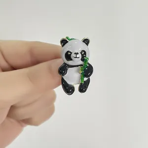 Cute panda brooch with green bamboo and gold trim held by hand to show compact size