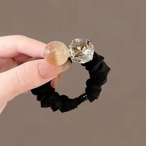 Dettaglio di elastico per capelli nero con perla ambrata e grande cristallo a taglio quadrato