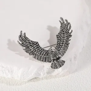 Minimalist antique silver eagle brooch with detailed feathers on a white stone background