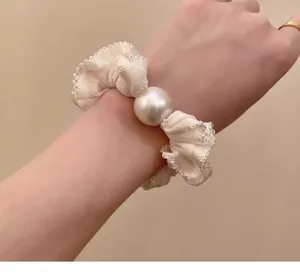 Detalle del coletero de encaje crema con adorno de perla grande para un estilo elegante