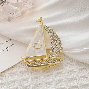 Detailweergave van een gouden zeilbootbroche met emaille en strass accenten