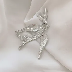 Silver swallow bird brooch with detailed feather texture on white silk fabric background
