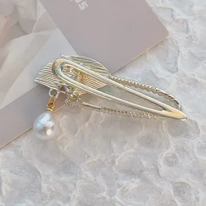 Elegant gold fan-shaped hair clip with white pearl drop pendant on textured background