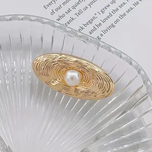 Détail d'une broche ovale dorée avec texture en spirale et perle centrale sur plat en verre