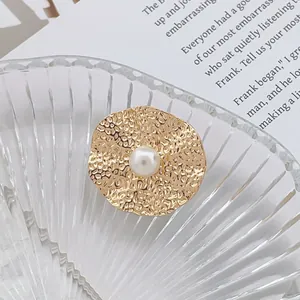 Détail macro d'une broche en métal doré martelé ornée d'une perle blanche centrale