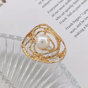 Détail d'une broche artistique dorée aux lignes tourbillonnantes avec une perle blanche