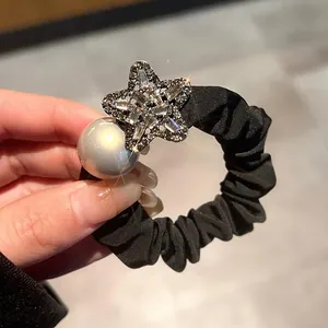 Detail view of black elastic hair tie with large grey pearl and sparkling zircon star