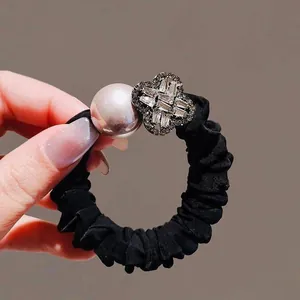 Detail of black scrunchie featuring faux pearls and sparkling clover charms with zircon