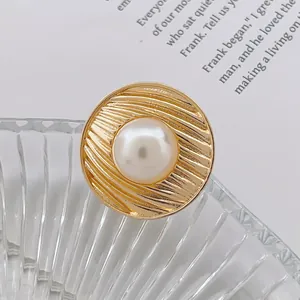 Détail d'une broche vintage dorée avec texture radiale et une perle blanche centrale
