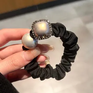 Detail of black fabric scrunchie with a gold rhinestone square and large white pearl