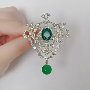 Elegant gold crown brooch with emerald stones and rhinestones in baroque style