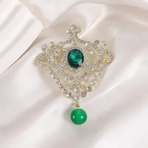 Detailed view of emerald green gemstone brooch with gold hollow crown and hanging bead