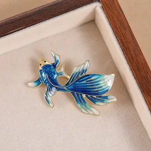 Detailed close-up of a blue enamel goldfish brooch with golden scales and fins in a gift box