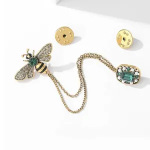 Elegant gold bee brooch with emerald gemstones and tassels on a clean white background