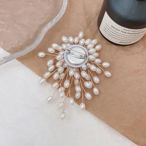 Handmade pearl flower brooch with gold wire and safety pin back on a warm backdrop