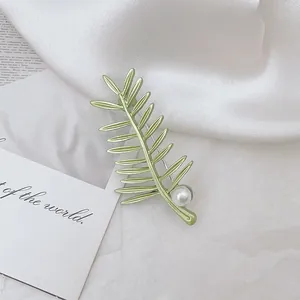 Vintage Brosche in Blattform Grün mit weißer Perle auf elegantem Satinhintergrund