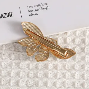 Golden butterfly hair clip with textured metallic wings on a clean white fabric background