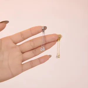 Detail of silver and gold huggie earrings featuring drop tassels with pear-cut zircon stones