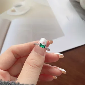 Detail of emerald cut green gemstone ring with small diamonds held by hand over coffee