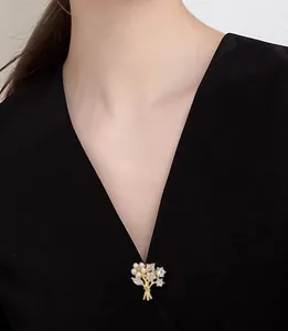 Close-up of a golden flower bouquet brooch with white pearls on a black V-neck top