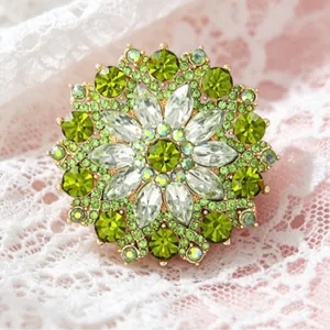 Elegant gold flower brooch with green and white crystals on a white lace background