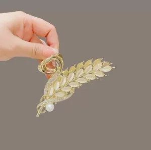 Detailed close-up of golden angel wing hair claw clip with cat eye stones and large pearl