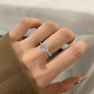 Close-up of a silver square-cut diamond ring with a pavé band worn on a finger