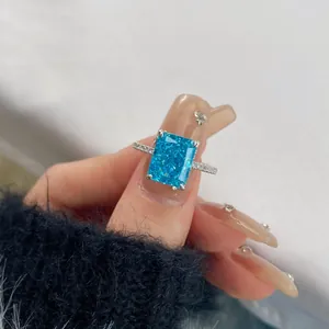 Close-up van rechthoekige blauwe aquamarijn zirkoon ring met zilveren pavé band om hand