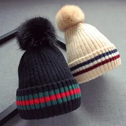 Détail de bonnets en laine tricotée noir et beige avec pompons et revers rayés colorés