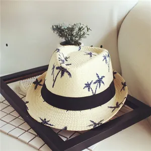 Detail of a beige straw hat featuring navy palm tree patterns and a black ribbon band