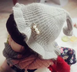 Détail du bonnet en tricot gris pour bébé avec pointe, bord volanté et broche perle étoile