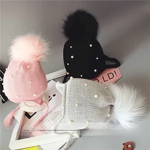 Détail de bonnets tricotés pour bébé avec pompons et perles en rose, noir et gris