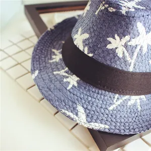 Detail of dark blue straw fedora hat featuring white coconut tree patterns and a black ribbon
